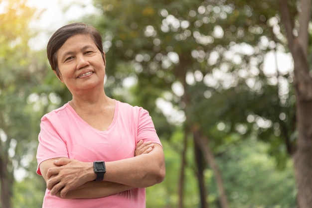 Asian Senior woman in pink shirt smiling with arms crossed before exercising.