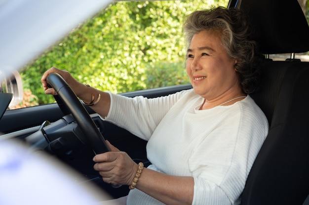 Asian senior woman smiling while driving car.