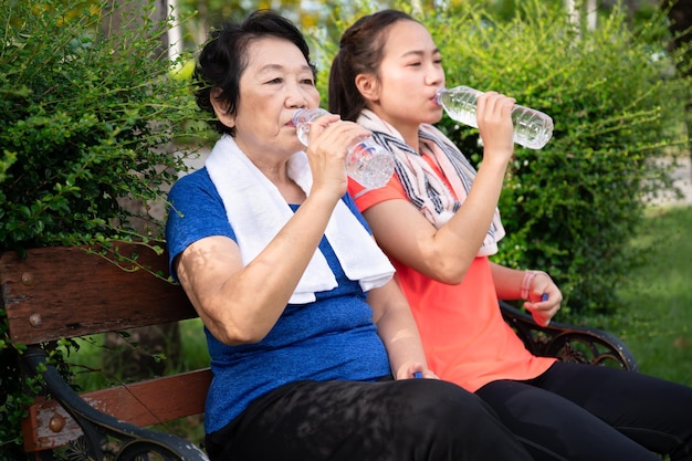 Asian senior woman and teenager rest with drinking pure water in plastic bottle after jogging