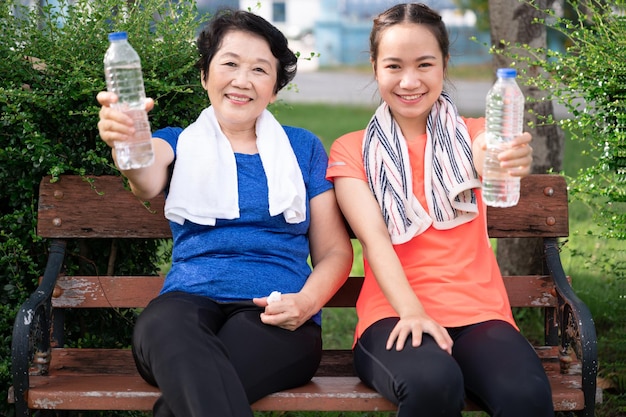 Asian senior woman and teenager rest with towel and pure water in plastic bottle after jogging