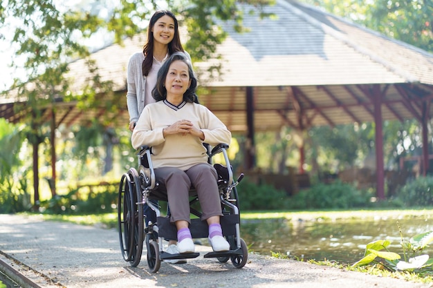 Asian senior woman in wheelchair with happy daughter Family relationship retired woman sitting on wheelchair in the park age care at retirement home