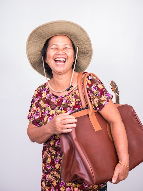 Asian senoir woman laughing while carrying ukulele and big brown bag