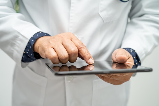 Asian smart man doctor holding digital tablet technology to search knowledge solve treatment for patient in hospital