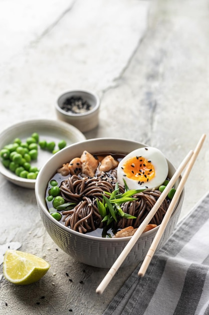 Asian soba noodle soup with chicken boiled egg sesame seeds green pea and green onion served with chopsticks Text space