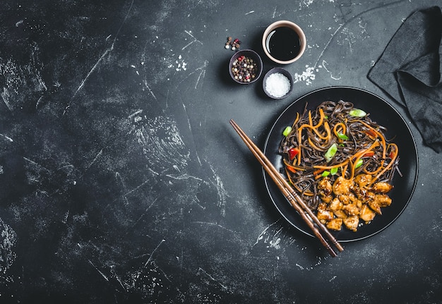 Asian soba noodles, chicken, vegetables, dark background. Space for text.