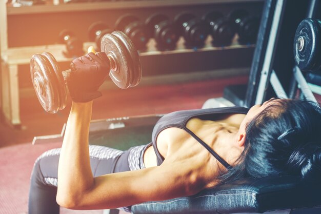 Asian sports woman doing exercises with dumbbell weights in gym