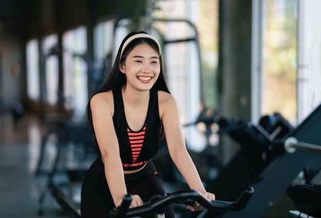 Asian sportswoman exercising on a bicycle in the gym determination to cardio lose weight makes her healthy exercise bike woman fitness sport concept