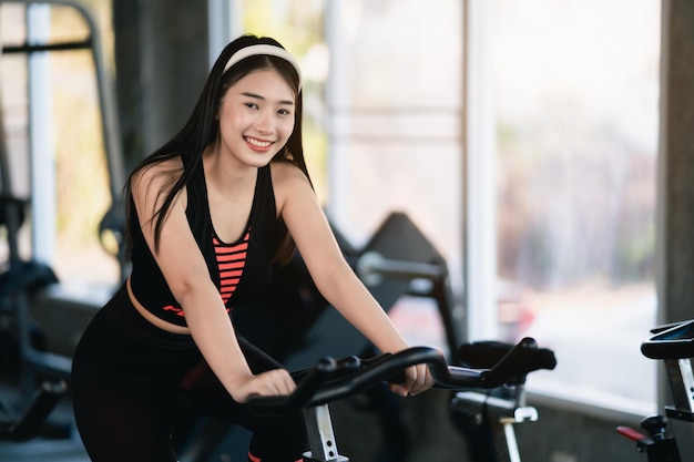 Asian sportswoman exercising on a bicycle in the gym determination to cardio lose weight makes her healthy exercise bike woman fitness sport concept