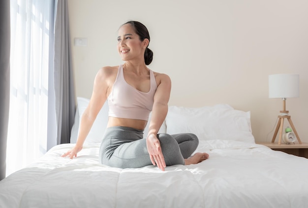 Asian sporty woman doing yoga exercise and stretching after waking up in morning on bed at home