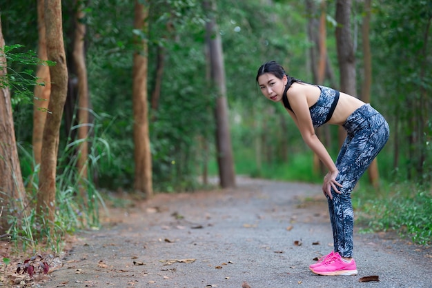 Asian sporty woman stretching body breathing fresh air in the parkThailand peopleFitness and exercise conceptJogging in the parkWarm up bodyTired from running