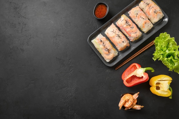 Asian spring rolls with colorful vegetables, prawn wrapped in rice paper on black background with copy space. View from above.