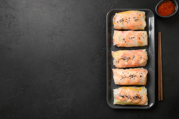 Asian spring rolls with prawn with spicy sauce wrapped in rice paper on black background with copy space. View from above.