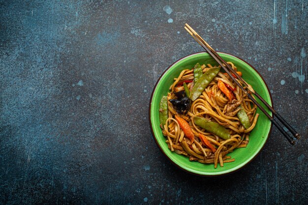 Asian stir fry noodles with chicken and veggies in green bowl top view