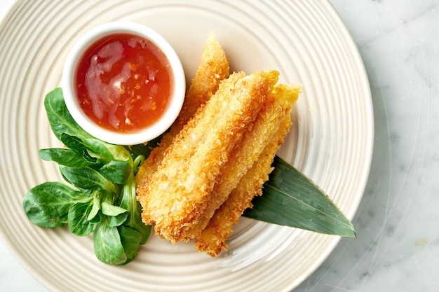 Asian street food - Deep-fried spring roll in rice paper served in a beige plate with spicy chili sauce on a marble table. Restaurant food.