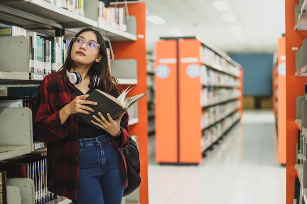 Asian student in casual style hold book while looking to side up to find another book at library