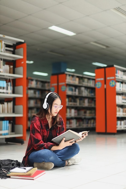 Asian student in casual style sitting on the library floor and reading a book while listening music