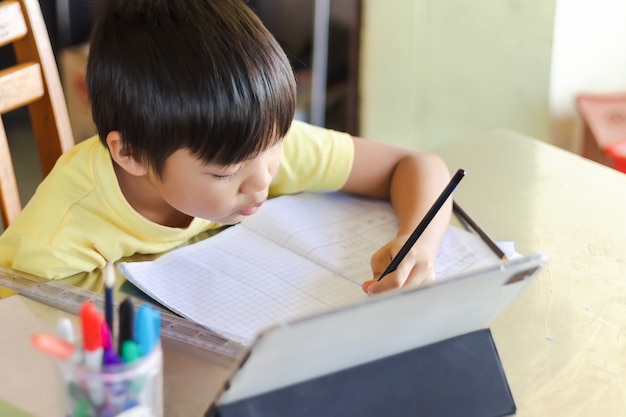 Asian student child boy using and touching smart pad or tablet for do his homework