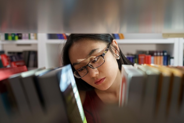 Asian student girl studying in university library young woman picking book from shelf for project