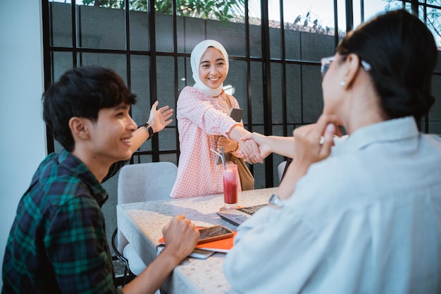 Asian student in hijab shaking hands with girl when meeting