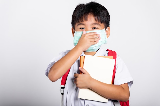 Asian student kid boy wearing student uniform and medical protect face mask and hand cover mouth