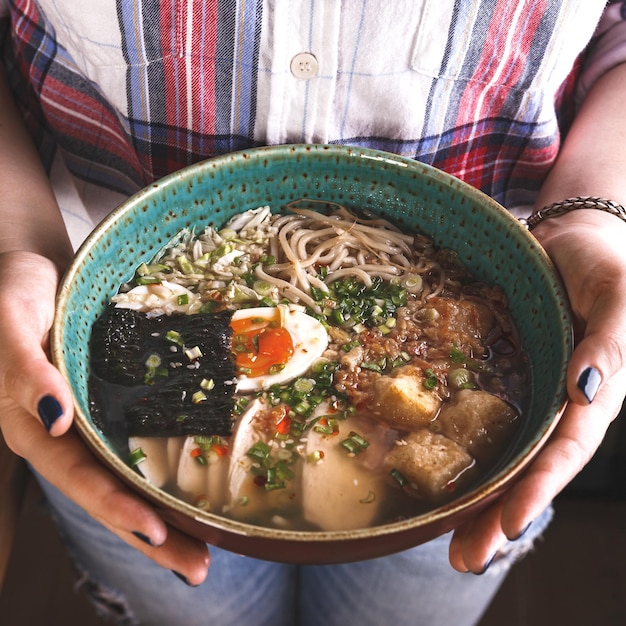 Asian style soup with noodles egg in bowl in the hands of young woman