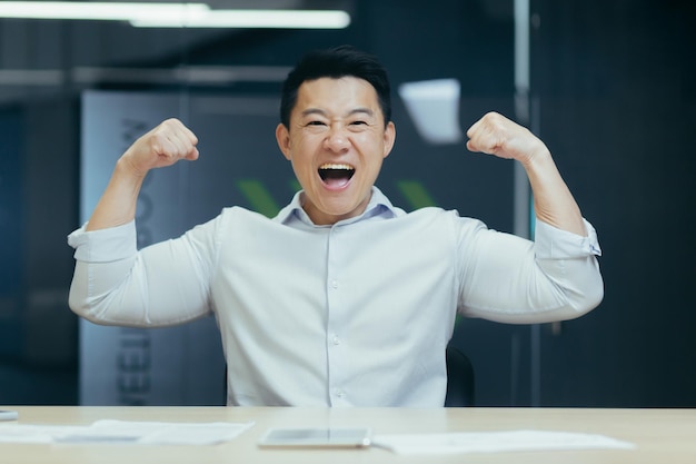 Asian super hero businessman looking at camera and smiling holding hands up gesture of strength