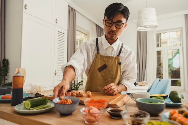 Asian sushi master making sushi rolls on a kitchen background ingredients for sushi on a table