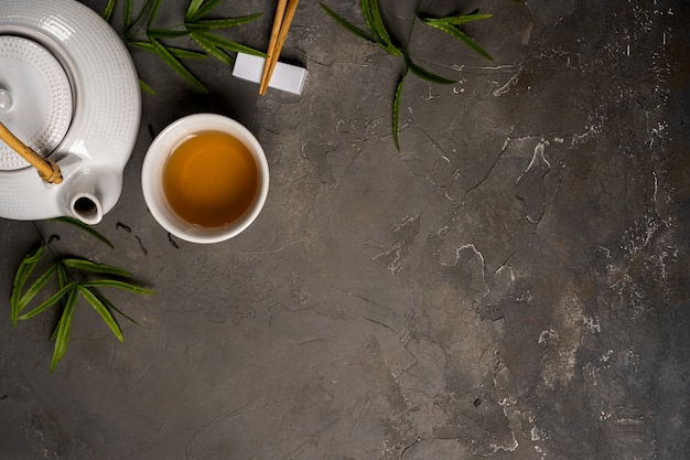 Asian tea concept, cup of tea and teapot surrounded with green tea dry leaves view from above