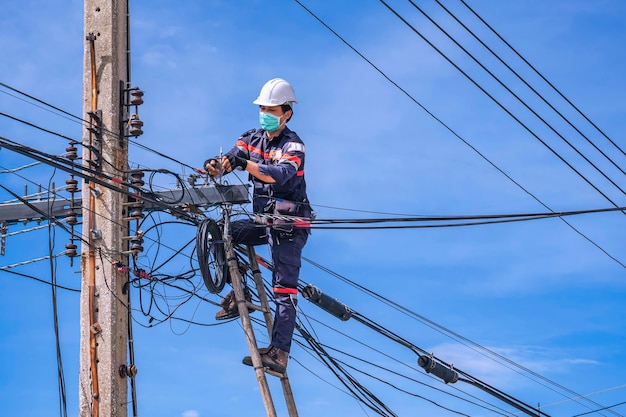 Asian technician on wooden ladder is installing internet fiber optic line on electric power pole