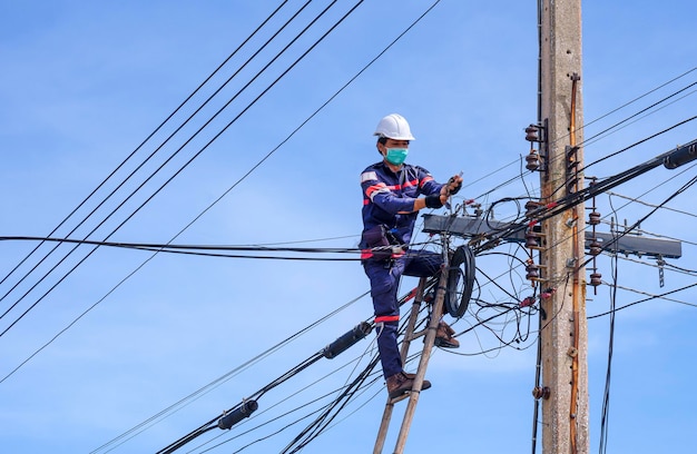 Asian technician on wooden ladder is installing internet fiber optic line on electric power pole