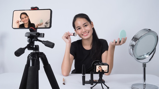 Asian teen woman sit in front of camera and live broadcasting as a beauty blogger influencer or youtuber to review or advice about how to make up at home. 