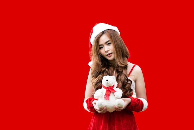 Asian teenage girl dressed as Santa Claus and holding a teddy bear Red background Christmas concept