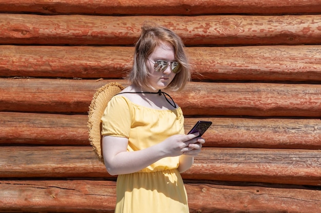 Asian teenage girl in yellow dress hat and sunglasses makes online shopping on phone communicates