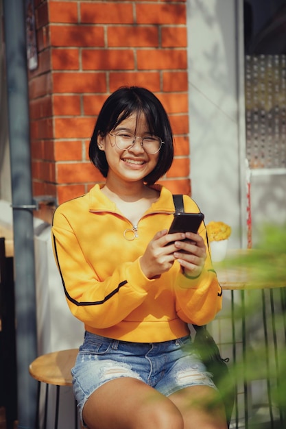 Asian teenager toothy smiling with happiness face with smartphone in hand sitting outdoor