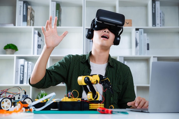 Asian teenager wearing VR glasses while experimenting robot arm project in house