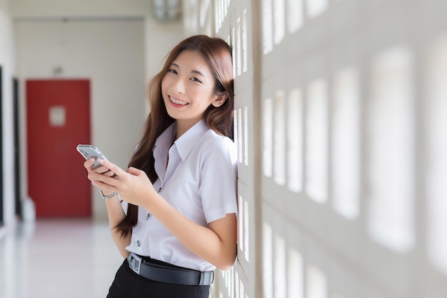 Asian Thai girl student in uniform is standing smiling happily and confidently while use smartphone