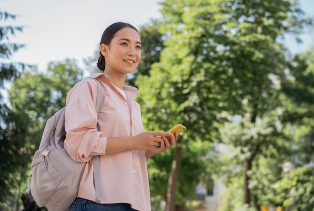 Asian tourist with backpack holding smartphone searching way walking in park