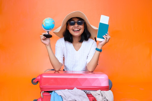 Asian tourist woman holding passport, boarding pass ticket and globe with opened suitcase. Travel co