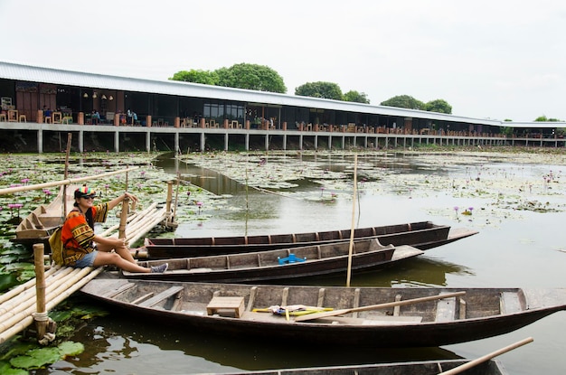 Asian travelers thai woman travel visit and sitting bamboo bridge for take photo with Wooden boat floating with water lily in pond at garden of Red Lotus floating market in Nakhon Pathom Thailand