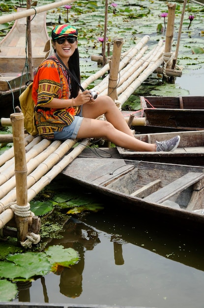 Asian travelers thai woman travel visit and sitting bamboo bridge for take photo with Wooden boat floating with water lily in pond at garden of Red Lotus floating market in Nakhon Pathom Thailand