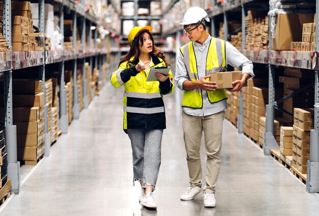 Asian two engineer team shipping order detail on tablet check goods and supplies on shelves with goods background inventory in factory warehouselogistic industry and business export