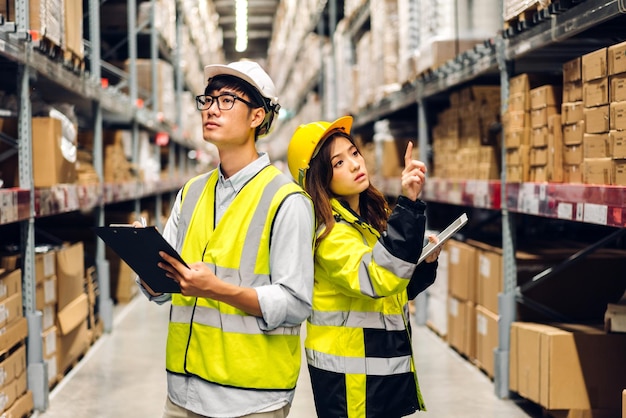 Asian two engineer team shipping order detail on tablet check goods and supplies on shelves with goods background inventory in factory warehouselogistic industry and business export