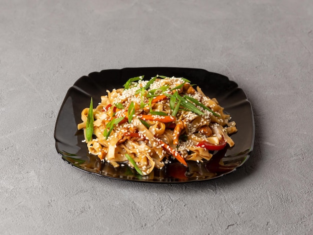 Asian vegetarian food udon noodles with mushrooms sesame and pepper closeup on a black plate