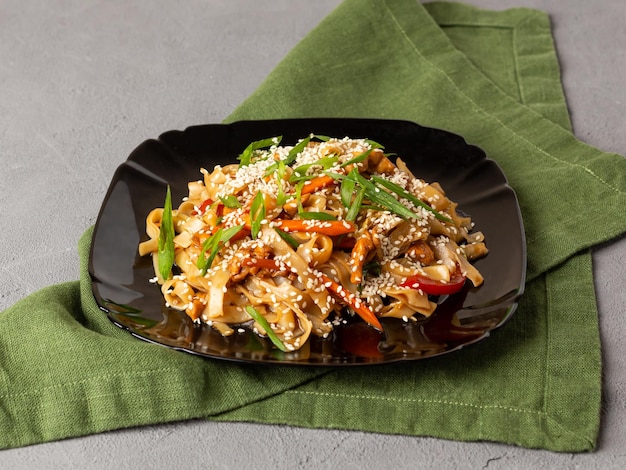 Asian vegetarian food udon noodles with mushrooms sesame and pepper closeup on a black plate