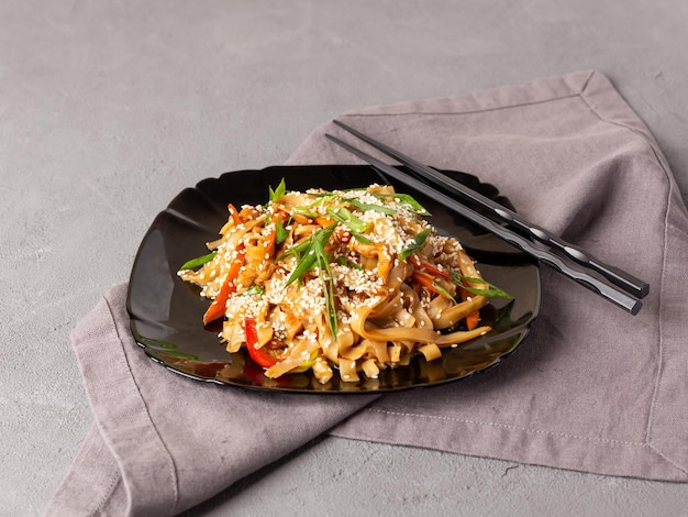 Asian vegetarian food udon noodles with mushrooms sesame and pepper closeup on a black plate