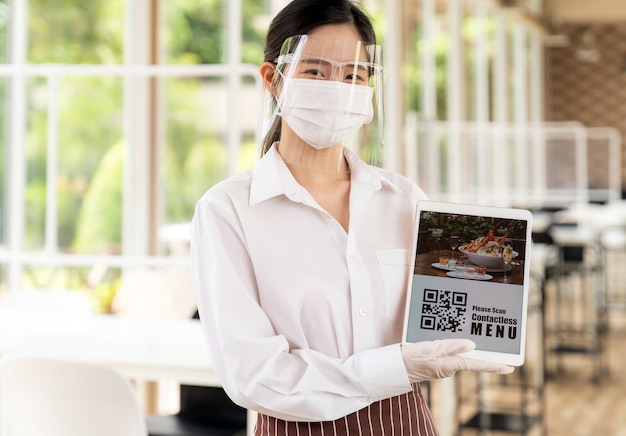 Asian waitress with face mask and face shield hold digital tablet with QR code