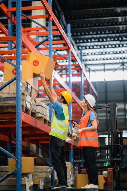 Asian warehouse workers lifting boxes on the shelf checking goods box shelf stock and standing on floklift in the warehouse factory storeworker barcode scaner check stock Warehouse Logistic concept