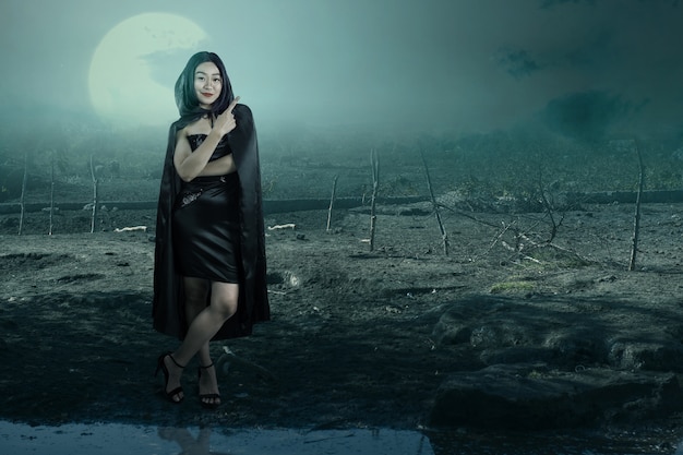 Asian witch woman with a cloak pointing something with the haunted field