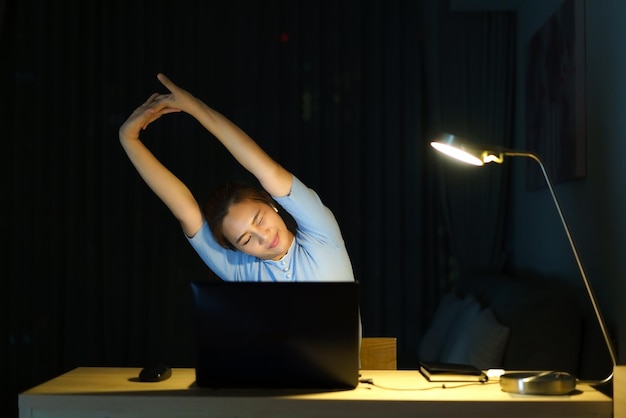 Asian woman are stretch lazily while working long hours in front of a computer in late night in living room at home