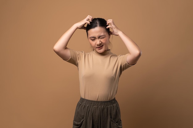 Asian woman bored and annoyed scratching her head standing isolated on beige background